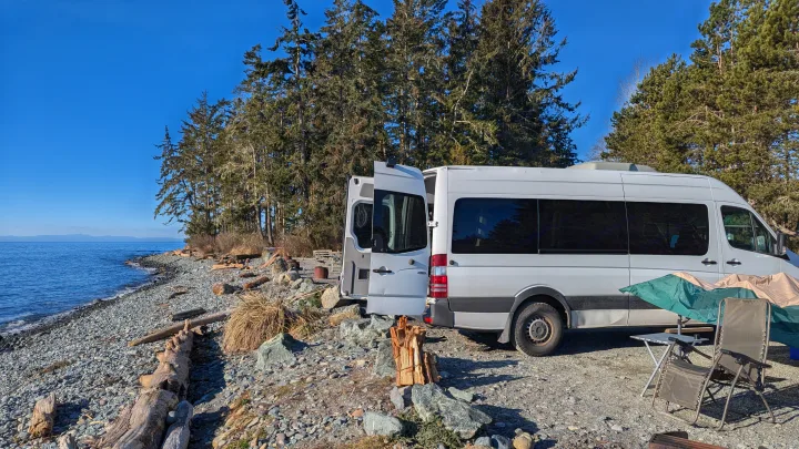 This white RV rental offers beachside camping by the calm ocean, with a cozy outdoor setup.. Mercedes Sprinter 2008