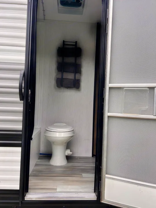 Clean RV rental bathroom showcasing a toilet, wall-mounted towel rack, and modern wood-look flooring. Essential amenities for mobile travel.. Heartland RVs Pioneer 2023