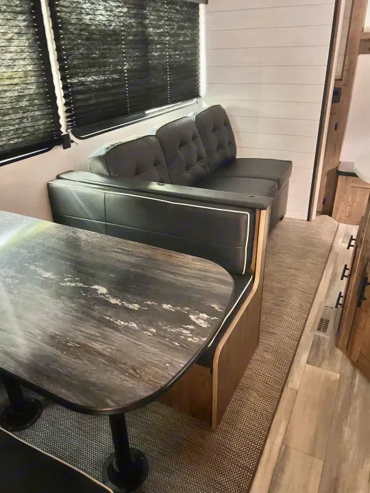 RV rental dinette: black tufted seating with white trim, a dark marbled table, and black pleated blinds.. Heartland RVs Pioneer 2023