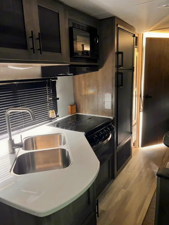 Inside an RV rental: a well-equipped kitchen with stainless steel sink, gas stove, microwave, and large fridge.. Heartland RVs Pioneer 2023