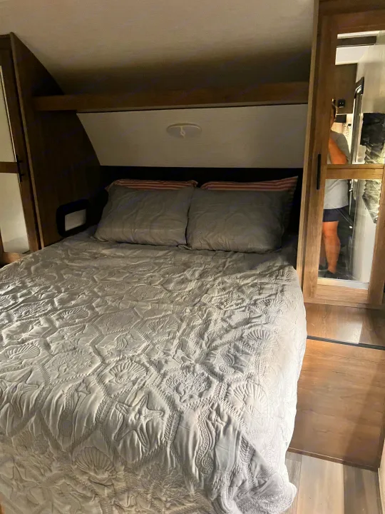 RV rental bedroom with a cozy bed featuring a quilted sea-themed comforter and mirrored closet visible.. Heartland RVs Pioneer 2023