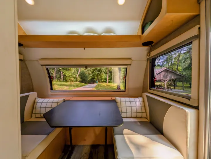 Experience nature from your RV rental! Bright dinette with a table, comfortable benches, and scenic windows revealing a wooded park.. Xtreme Outdoors Little Guy Max 2021