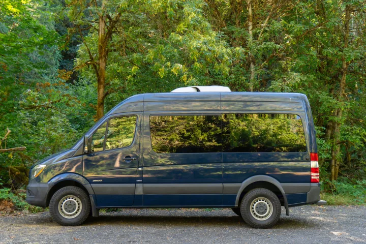 Dark blue Mercedes Sprinter RV rental parked in a lush green forest, ready for outdoor adventure.. Mercedes-Benz Sprinter 2016