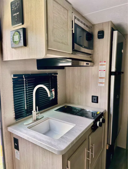 This RV rental's modern kitchenette, with sink, cooktop, microwave, and fridge, offers compact convenience for travel.. Coachmen Catalina 2023