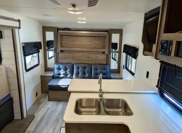 RV rental interior showcasing a bright kitchen, black sofa, and fold-down bed.. Heartland RVs Pioneer 2023