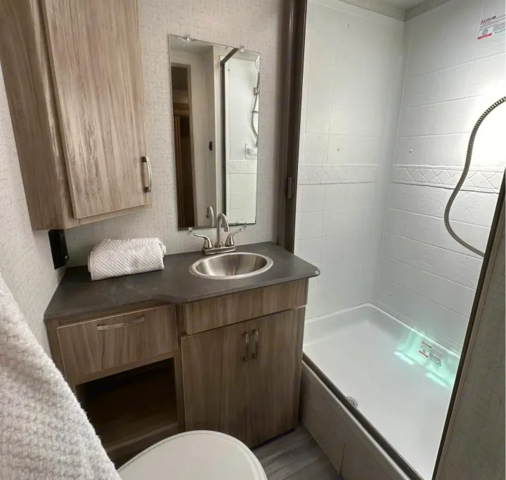 Clean RV rental bathroom with a vanity, sink, mirror, shower, and toilet for a comfortable stay.. Minnie Minnie Trailer 2022