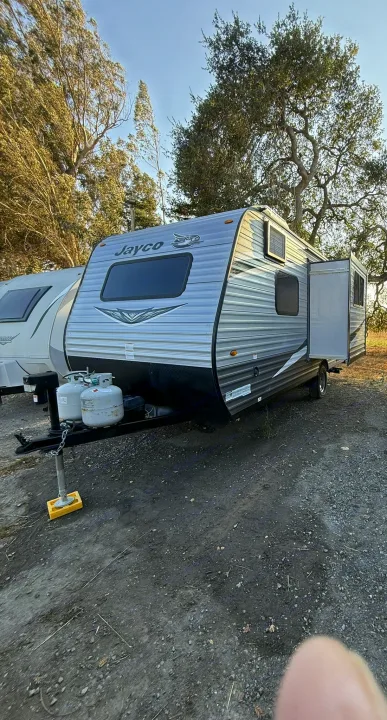 Jayco travel trailer RV rental: A silver unit with propane tanks, parked on gravel in a natural setting.. Jayco Jay Flight SLX 2021