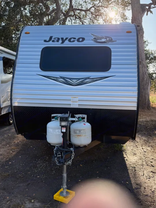 Full front view of a grey Jayco travel trailer, an RV rental, showing its logo, window, propane tanks, and hitch.. Jayco Jay Flight SLX 2021