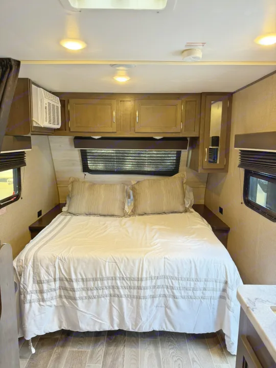 Comfortable RV rental bedroom with a large bed, overhead cabinets, AC, and windows for a relaxing trip.. Jayco Jay Flight SLX 2021