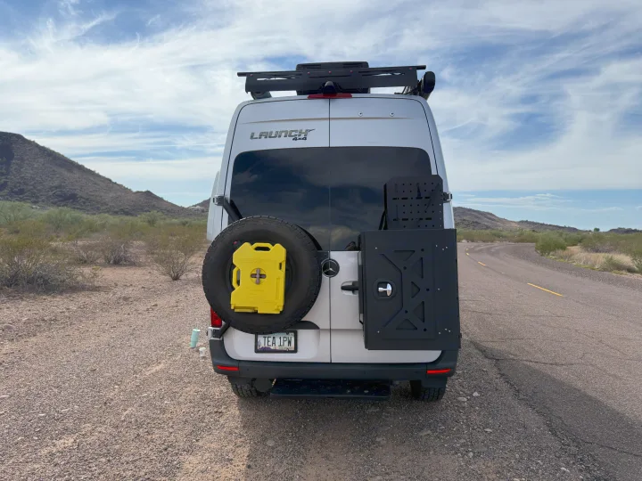 White Launch 4x4 rv rental van with spare tire, yellow fuel pack, and cargo mount, ready for desert adventures.. Entegra Coach Launch 2023