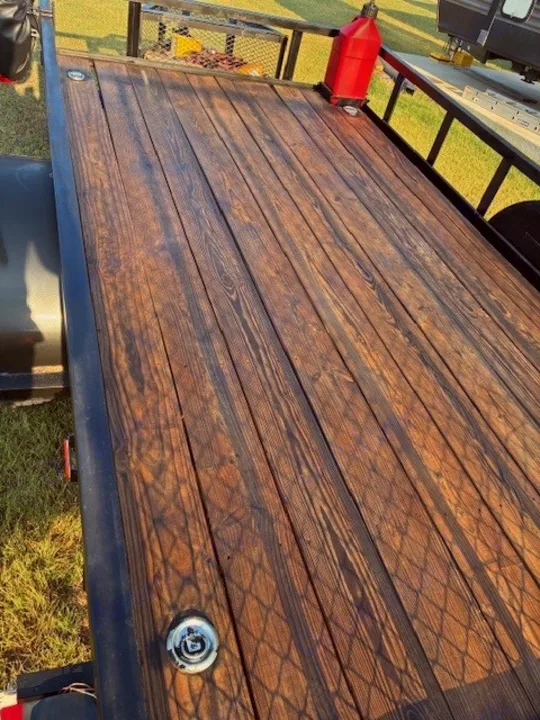 Durable wooden trailer deck, possibly for an rv rental, with a red gas can, tie-downs, and an RV beyond.. Carry On Trailers 6X12GWPTLED 2022