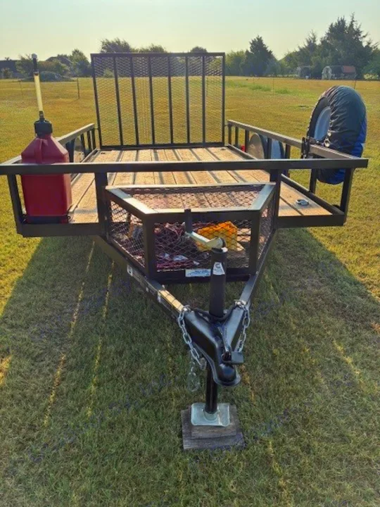 Black utility trailer with wooden deck, front mesh gate, gas can, & spare tire. Perfect for hauling gear for your RV rental trip.. Carry On Trailers 6X12GWPTLED 2022