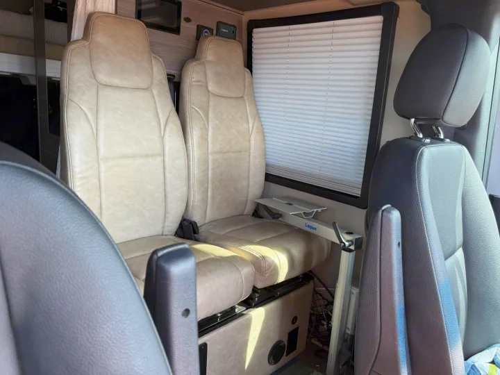 RV rental interior: beige swivel seats, window with blind, and a Lagun table mount for flexible space.. Entegra Coach Launch 2023