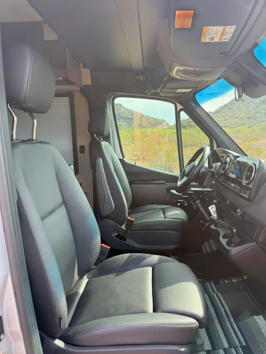 RV rental front cabin interior with black leather seats, modern dashboard, and desert mountain views through the windows.. Entegra Coach Launch 2023