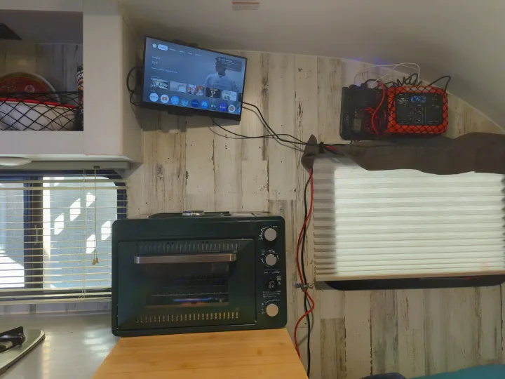 This RV rental's compact interior features a TV displaying F1, a green mini-oven, and an orange portable power station.. Travel Lite Rove Lite 2023