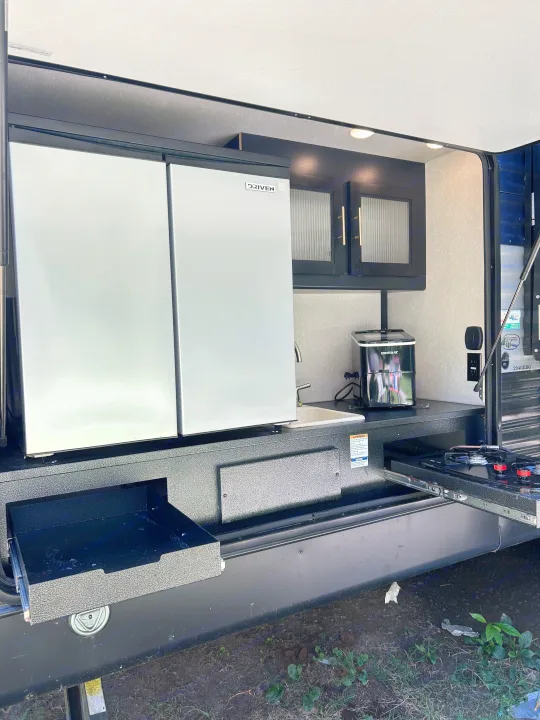 An RV rental's sleek outdoor kitchen featuring a fridge, sink, ice maker, and a convenient pull-out stove.. Forest River Cherokee 2021