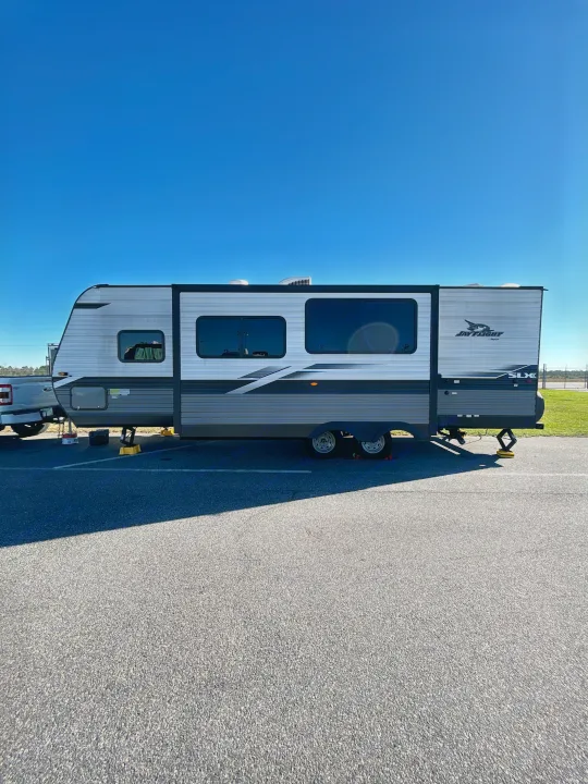 A Jay Flight SLX travel trailer, perfect for your next rv rental, parked on a paved lot under a clear blue sky. Truck visible.. Jayco Jay Flight 2022