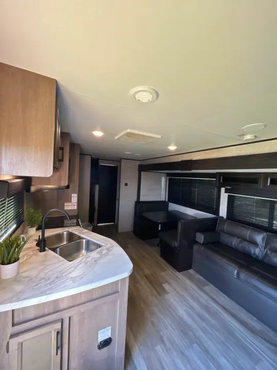Bright rv rental interior: modern kitchen with double sink, dining booth, and a comfy black sofa living area.. Jayco Jay Flight 2022