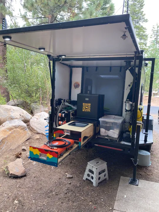 Explore this RV rental: a compact camper's rear reveals a convenient outdoor kitchen with a pull-out stove, sink, and fridge at a scenic campsite.. ITWO custom Pixtech Bearlander 20 2024