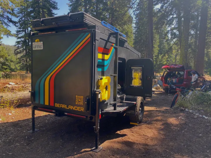 An overland trailer, ideal for RV rental adventures, is parked at a sunny forest campsite next to an SUV.. ITWO custom Pixtech Bearlander 20 2024