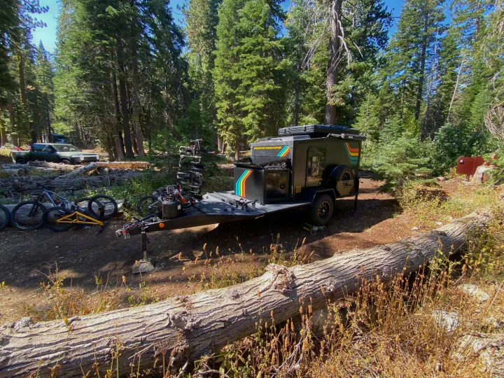 Dark grey overland trailer for RV rental parked in a sunny forest campsite with bikes and a Rivian. Ready for outdoor adventures.. ITWO custom Pixtech Bearlander 20 2024