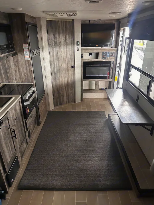RV rental interior: kitchen with stove & fridge, TV, electric fireplace, and adaptable dining bench by the entry. Perfect for travel.. Forest River Salem 2021