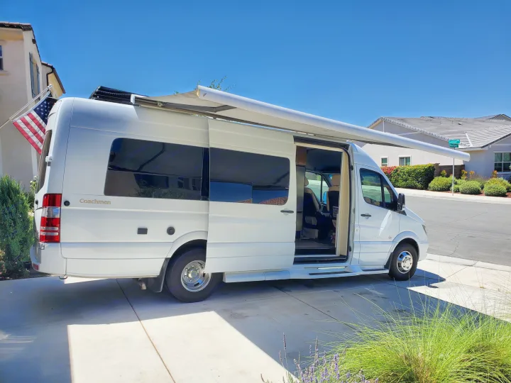 White Coachmen Galleria camper van, a popular RV rental option, parked with an extended awning and open door.. Coachmen Galleria 2019