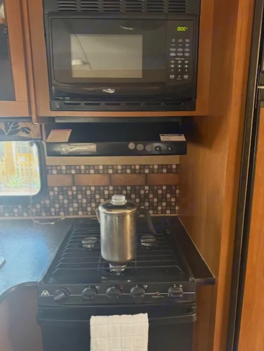 RV rental kitchen featuring a microwave, range, tiled backsplash, and a coffee percolator on the stovetop.. StarCraft Autumn Ridge 2013