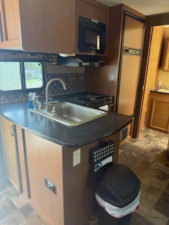 A compact RV rental kitchen with a sink, stove, microwave, and refrigerator, offering essential amenities.. StarCraft Autumn Ridge 2013