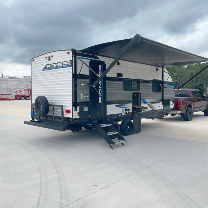 Cloudy sky over an RV rental travel trailer with awning extended, hitched to a dark pickup truck.. Heartland RVs Pioneer 2023