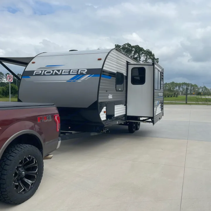 An RV rental - a Pioneer travel trailer - hitched to a Ford FX4 pickup, parked on concrete under a cloudy sky.. Heartland RVs Pioneer 2023