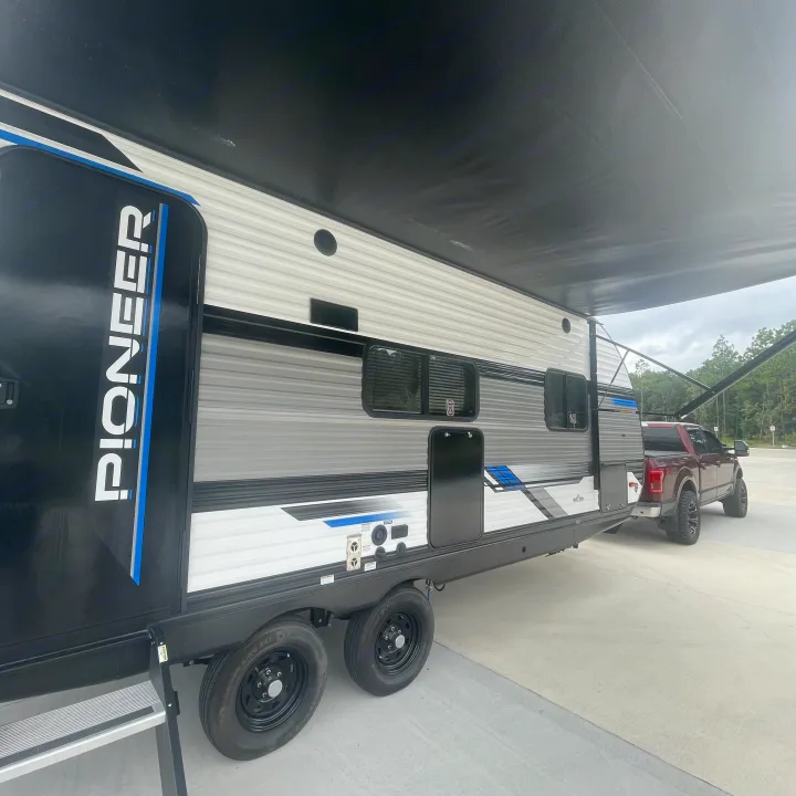 A sleek, modern rv rental travel trailer, branded 'PIONEER,' with an extended awning, is hitched to a red pickup truck.. Heartland RVs Pioneer 2023