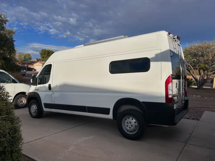 White Ram ProMaster RV rental van with a roof AC and rear ladder, parked in a residential driveway under a cloudy sky.. Ram Promaster 2500 2022
