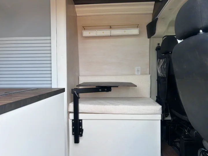 RV rental interior: light wood, white cushions, folding table, and storage drawers. Features a power outlet for compact travel.. Ram Promaster 2500 2022