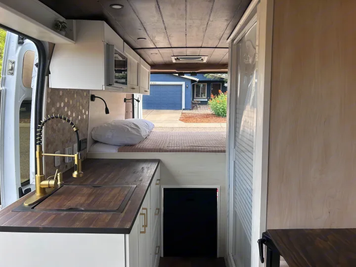 RV rental interior featuring a full kitchen with brass faucet, wooden counter, comfy bed area, and a compact shower.. Ram Promaster 2500 2022