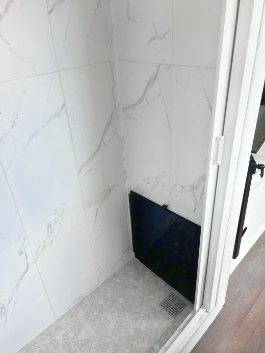 Peek inside an RV rental's shower: white marble-style walls, gray hexagonal floor, and a sleek black storage panel.. Ram Promaster 2500 2022