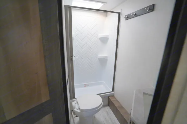 View of a modern RV rental bathroom, showcasing a white toilet, enclosed shower with herringbone pattern, and vanity.. Forest River Surveyor Legend 2022