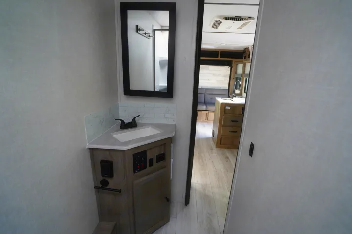 This compact RV rental features a modern bathroom vanity with sink & mirror, revealing kitchen and living areas through the doorway.. Forest River Surveyor Legend 2022