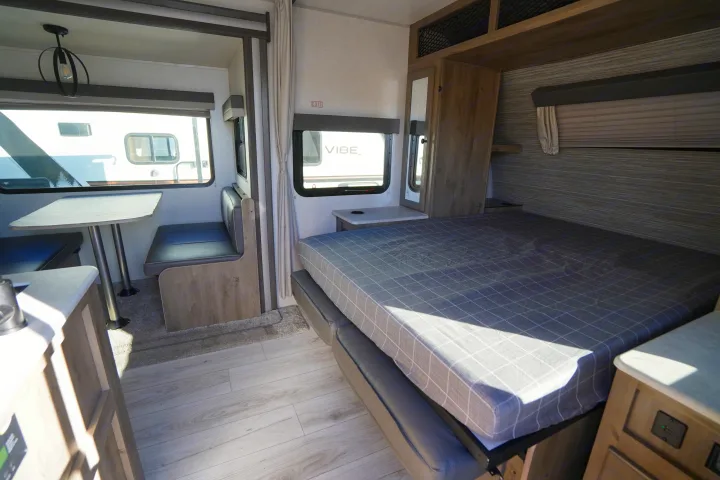 RV rental interior with dinette, plaid-covered bed, and light wood cabinetry. Large windows let in natural light.. Forest River Surveyor Legend 2022