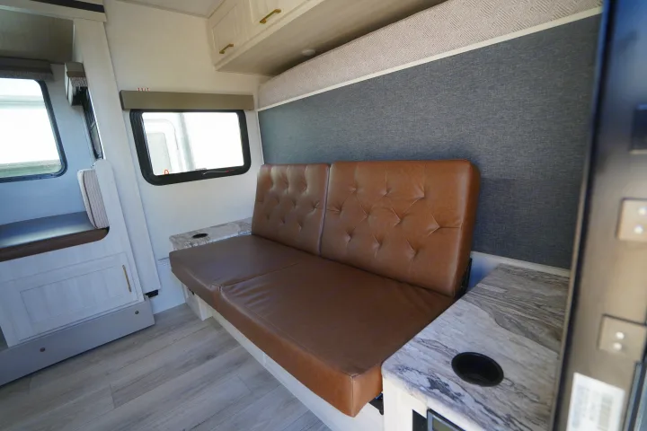 Step inside this RV rental's inviting living space, featuring a brown tufted sofa, dinette, and light wood cabinetry.. Forest River Surveyor Legend 2024