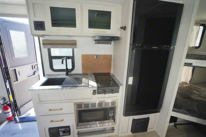 Modern rv rental kitchen with sink, stove, microwave, large fridge, and adjacent bunk beds.. Forest River Surveyor Legend 2024