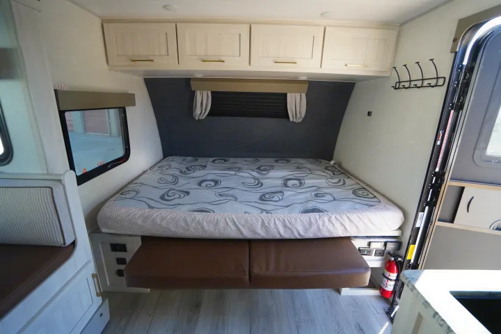 This **RV rental** features a compact bedroom: bright overhead cabinets, a patterned bed, and versatile seating.. Forest River Surveyor Legend 2024