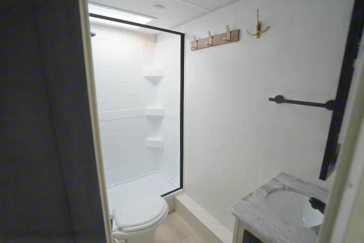 Compact RV rental bathroom with white shower, toilet, and modern sink vanity. Wall hooks offer practical storage.. Forest River Surveyor Legend 2024