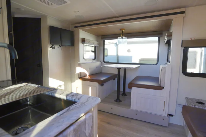 Spacious and modern RV rental interior featuring a kitchen sink, dinette booth with table, and large windows. Perfect for travel!. Forest River Surveyor Legend 2024