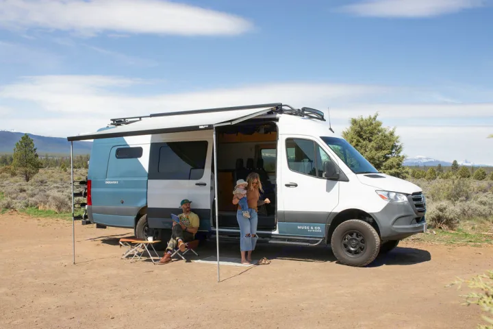 An rv rental camper van provides outdoor comfort for a family; parents and baby relax under an extended awning.. Mercedes-Benz Sprinter 2020