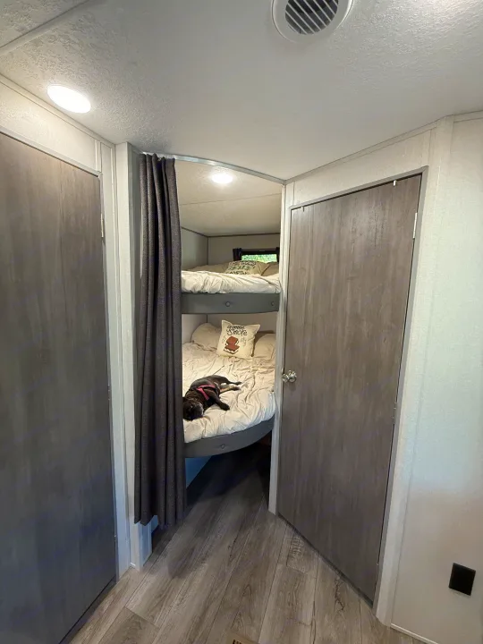 Cozy RV rental bunk beds with comfy pillows, a sleeping black dog, and modern interior finishes make for happy camping.. Coachmen Catalina 261BHS 2025
