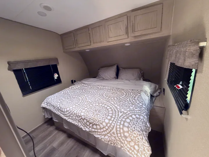 Cozy RV rental bedroom with a comfy bed, overhead cabinets, and windows, perfect for your next adventure.. Coachmen Catalina 2022
