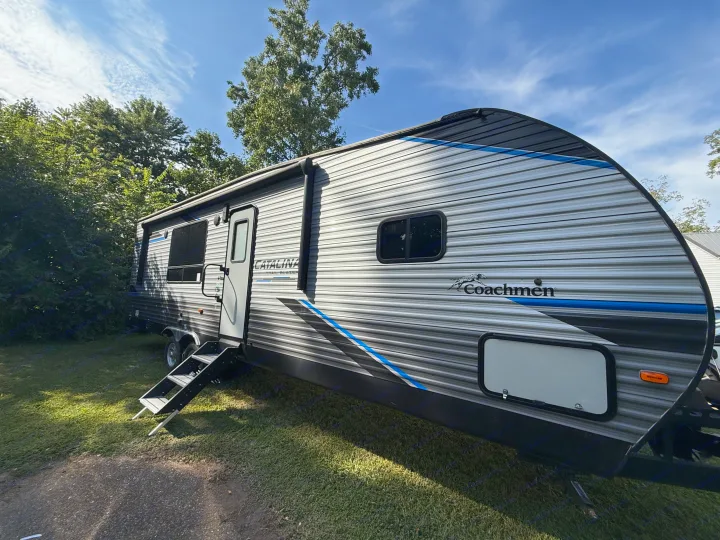 A grey & blue Coachmen RV rental with open door & steps, parked on green grass. Perfect for your next travel trailer adventure.. Coachmen Catalina 2022
