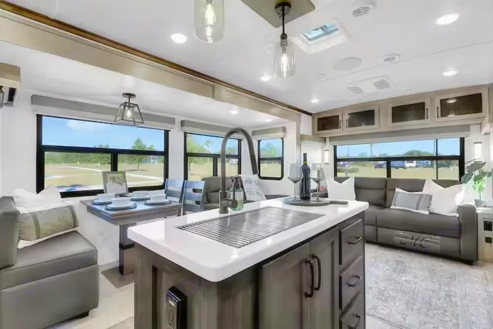 Interior of a modern RV rental featuring a kitchen island, dining table, and cozy living area with large windows.. Forest River Flagstaff Classic 2024