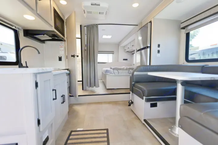 Modern RV rental interior showing a kitchen, dining booth, and private bedroom with bright lighting.. Coachmen Freelander 2023